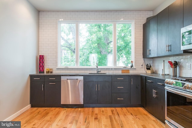 kitchen with sink, dark stone counters, light hardwood / wood-style floors, decorative backsplash, and appliances with stainless steel finishes