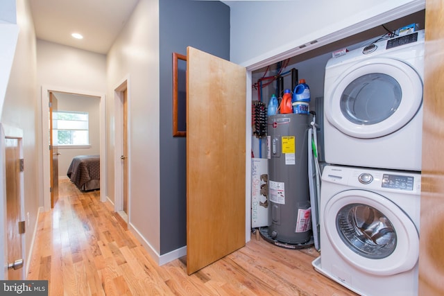 clothes washing area with water heater, stacked washer and dryer, and light hardwood / wood-style flooring