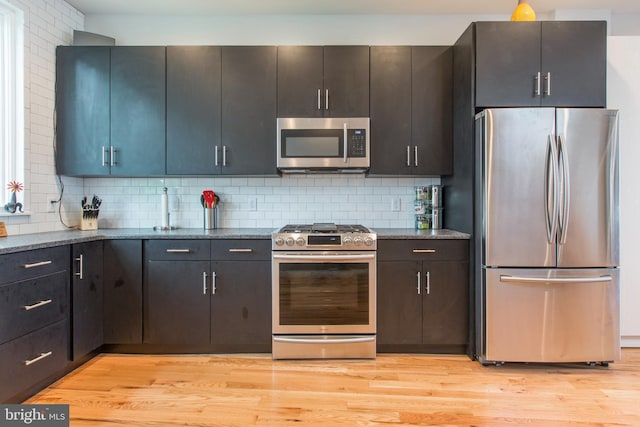 kitchen featuring backsplash, stainless steel appliances, dark stone counters, and light hardwood / wood-style flooring