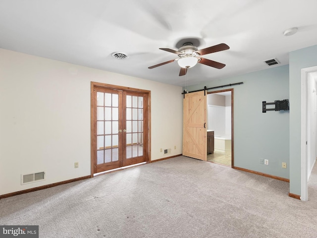 unfurnished bedroom featuring connected bathroom, a barn door, light colored carpet, ceiling fan, and french doors