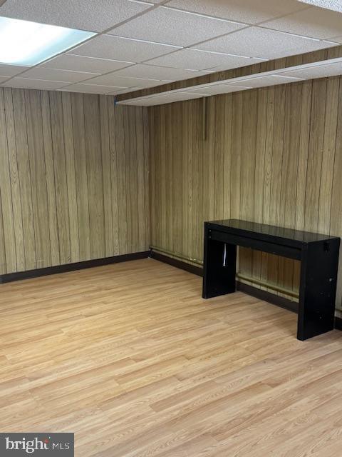 interior space featuring a drop ceiling, light hardwood / wood-style flooring, and wooden walls