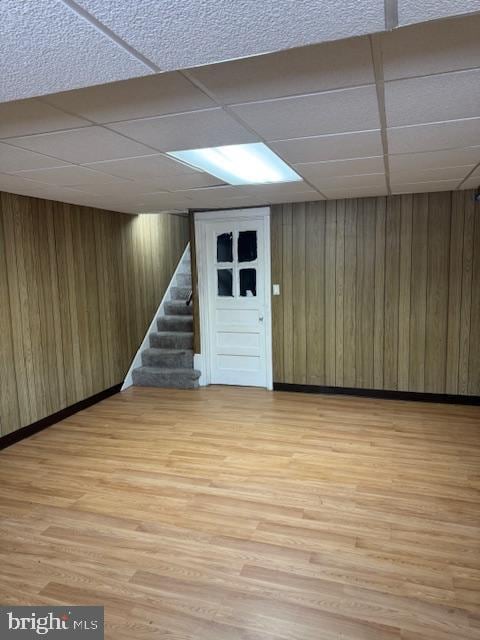 basement with a paneled ceiling, hardwood / wood-style floors, and wooden walls