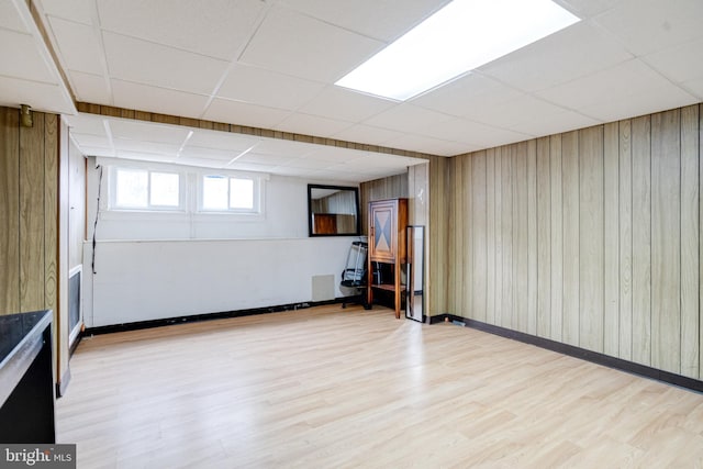 basement featuring a paneled ceiling, wood walls, and light hardwood / wood-style flooring