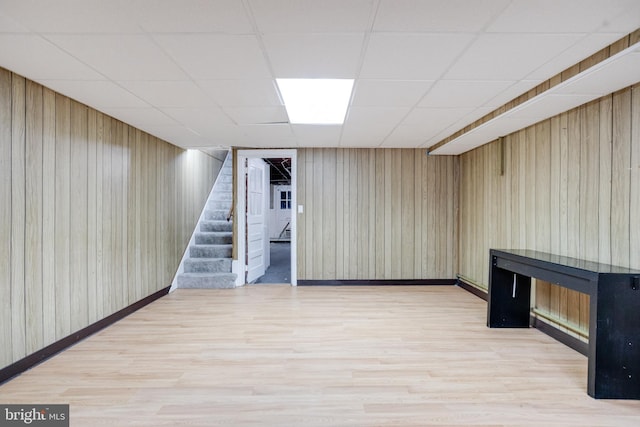 basement featuring a paneled ceiling, wood walls, and light hardwood / wood-style flooring