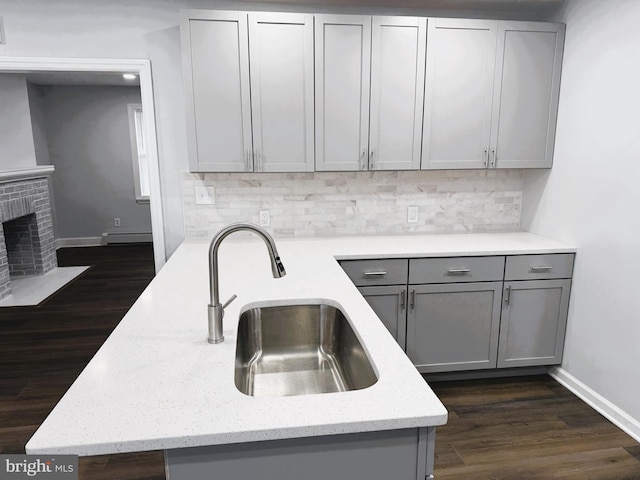 kitchen with gray cabinets, a baseboard heating unit, decorative backsplash, light stone countertops, and sink