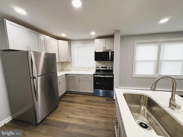 kitchen featuring stainless steel appliances, sink, backsplash, dark hardwood / wood-style floors, and light stone counters