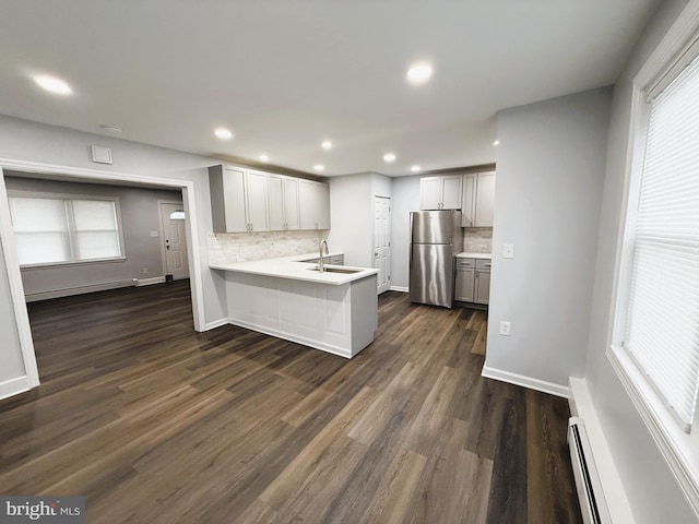 kitchen with dark hardwood / wood-style floors, kitchen peninsula, decorative backsplash, stainless steel refrigerator, and a baseboard radiator