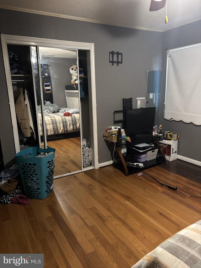 bedroom with crown molding, ceiling fan, wood-type flooring, and a closet