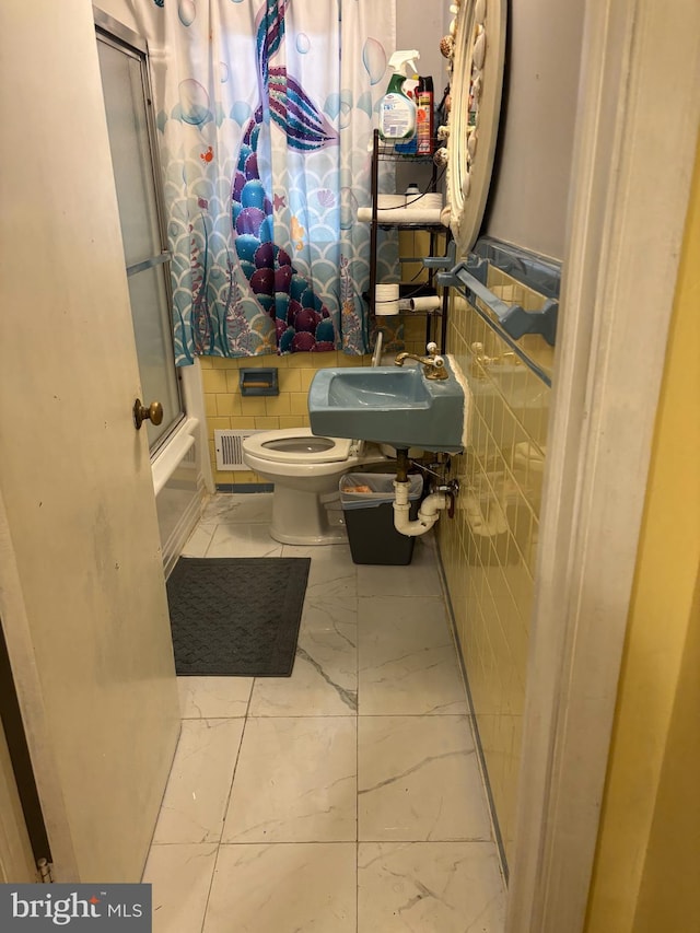 full bathroom featuring tile walls, sink, bath / shower combo with glass door, and toilet