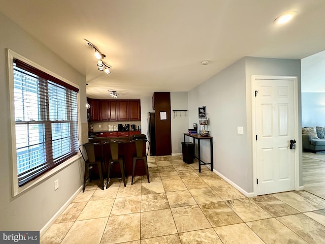 kitchen with stainless steel fridge, track lighting, light tile patterned floors, and a kitchen breakfast bar