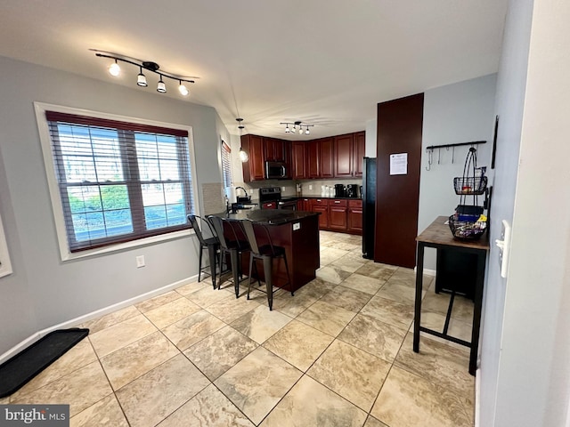 kitchen with appliances with stainless steel finishes, sink, light tile patterned floors, hanging light fixtures, and a breakfast bar area