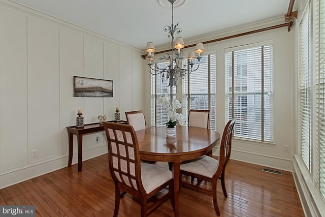 dining area featuring wood-type flooring, an inviting chandelier, ornamental molding, and a healthy amount of sunlight