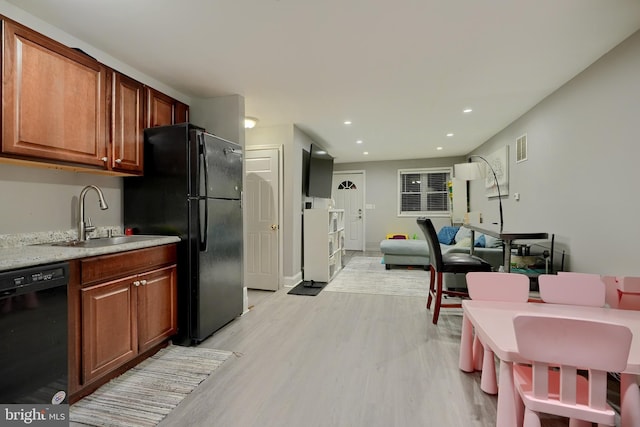 kitchen with light hardwood / wood-style floors, sink, light stone counters, and black appliances