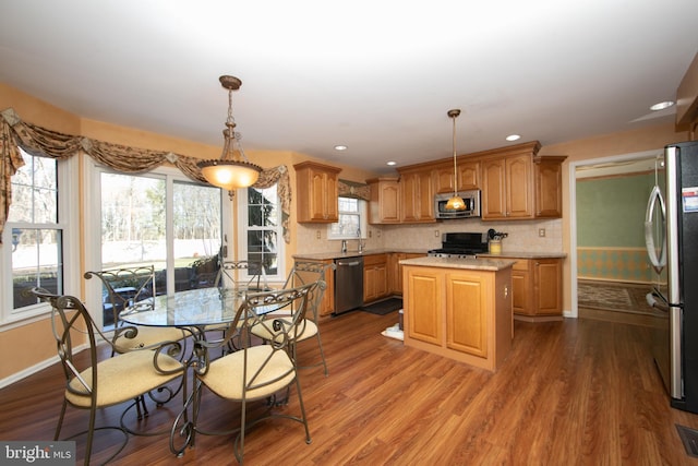 kitchen featuring appliances with stainless steel finishes, tasteful backsplash, wood-type flooring, hanging light fixtures, and a center island