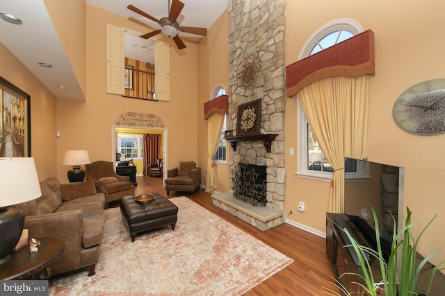 living room with a high ceiling, ceiling fan, hardwood / wood-style flooring, and a stone fireplace