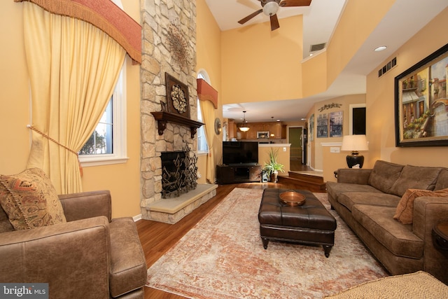 living room featuring a high ceiling, ceiling fan, a fireplace, and hardwood / wood-style floors