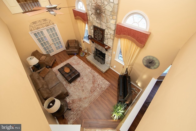 living room featuring ceiling fan, a high ceiling, wood-type flooring, and a fireplace