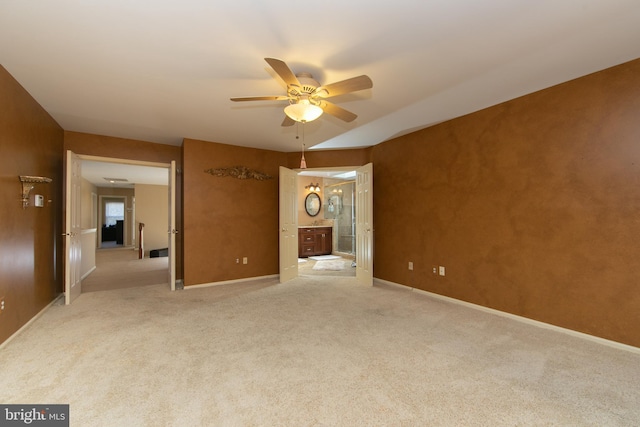 interior space featuring ceiling fan, light colored carpet, and ensuite bath