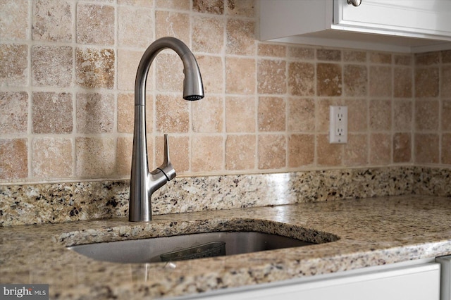 room details featuring light stone countertops, white cabinets, and sink