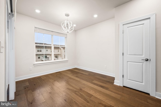 spare room featuring a chandelier and dark wood-type flooring