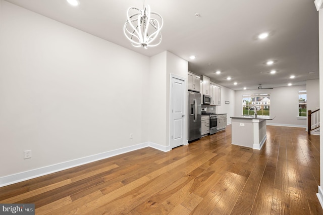 kitchen with stainless steel appliances, a kitchen island with sink, sink, an inviting chandelier, and white cabinetry