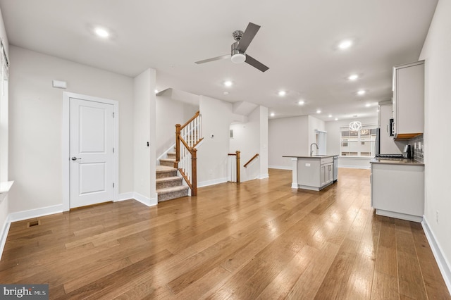 unfurnished living room with ceiling fan, sink, and light wood-type flooring