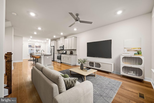 living room with ceiling fan, light hardwood / wood-style flooring, and sink