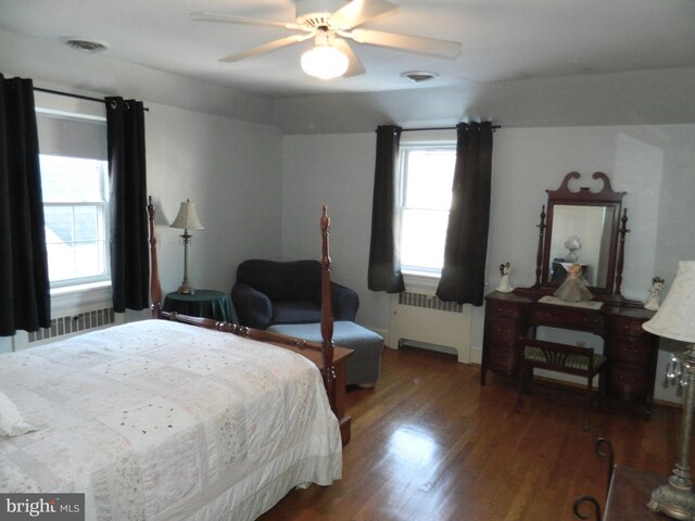 bedroom with multiple windows, dark wood-type flooring, radiator heating unit, and ceiling fan