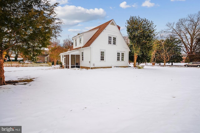 snow covered rear of property with a sunroom