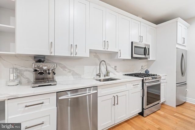 kitchen with stainless steel appliances, light wood-type flooring, light stone countertops, sink, and white cabinetry