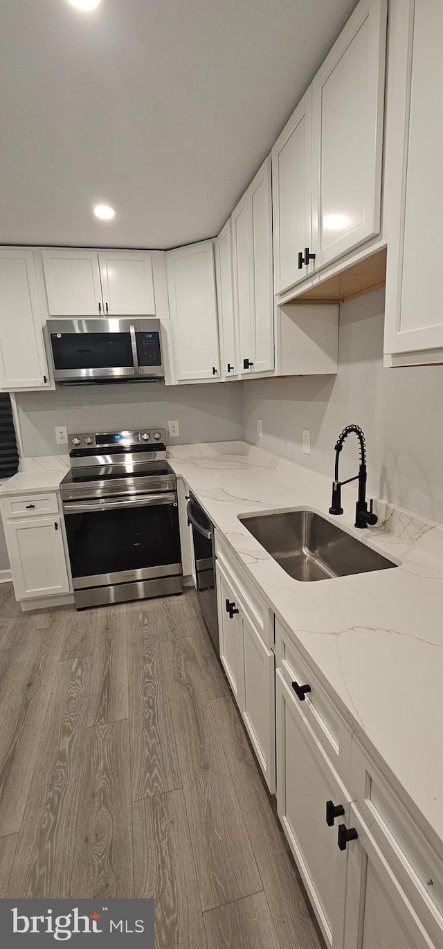 kitchen with white cabinets, appliances with stainless steel finishes, sink, hardwood / wood-style flooring, and light stone counters