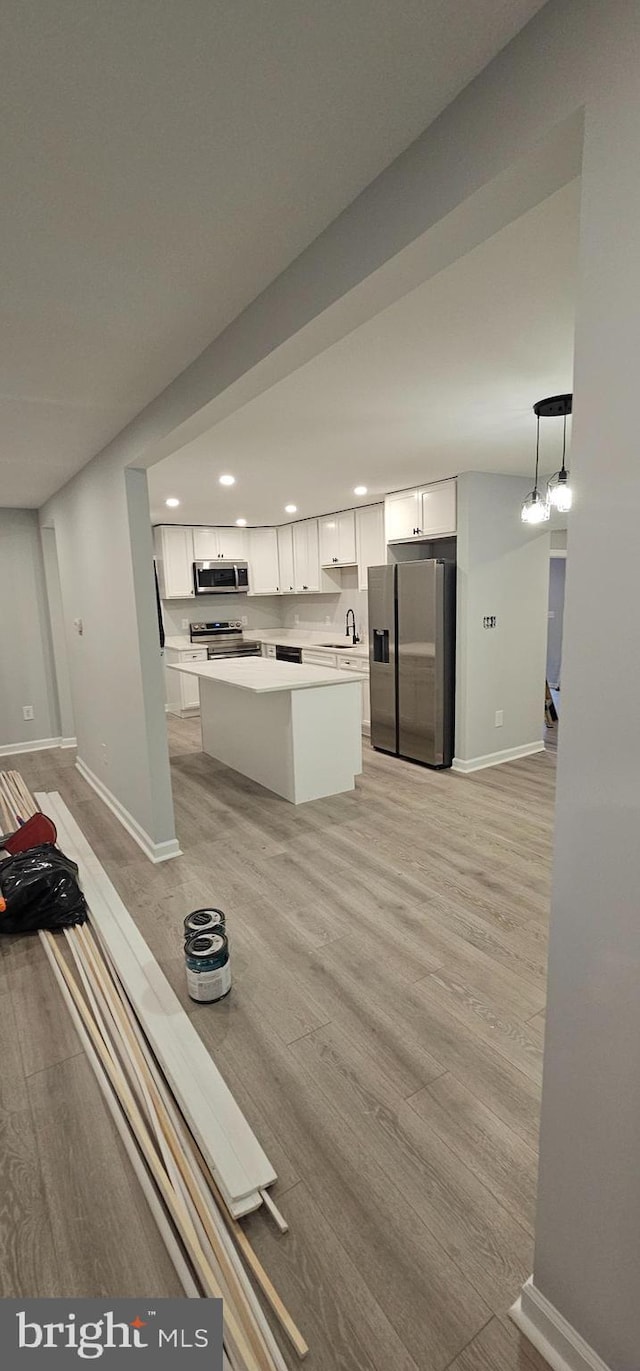 kitchen featuring decorative light fixtures, white cabinetry, stainless steel appliances, sink, and light wood-type flooring