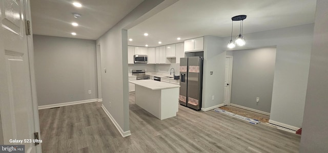 kitchen with pendant lighting, a kitchen island, light hardwood / wood-style flooring, stainless steel appliances, and white cabinets