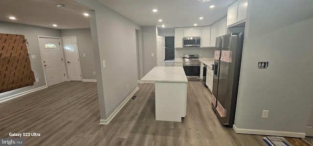 kitchen featuring white cabinetry, stainless steel appliances, wood-type flooring, light stone countertops, and a kitchen island