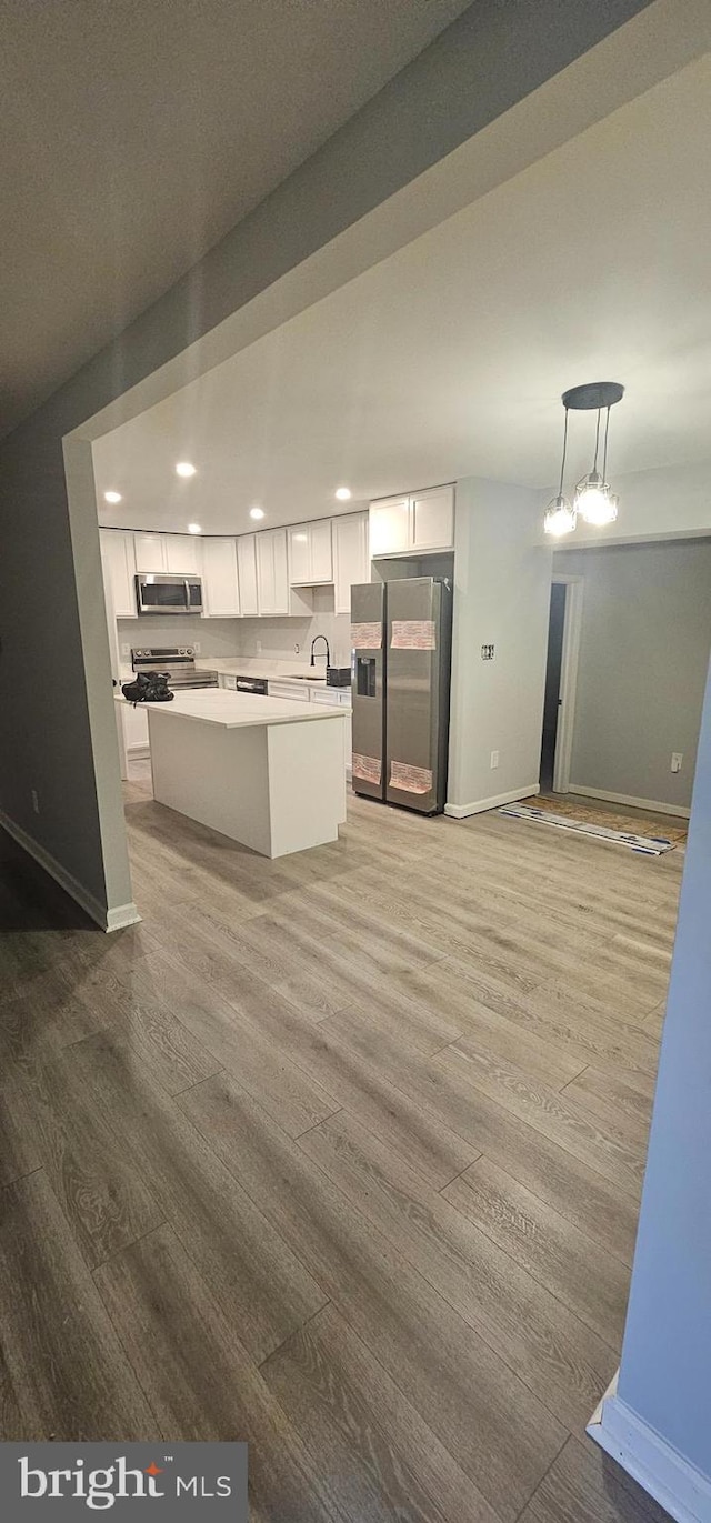 kitchen with a center island, wood-type flooring, white cabinetry, hanging light fixtures, and stainless steel appliances