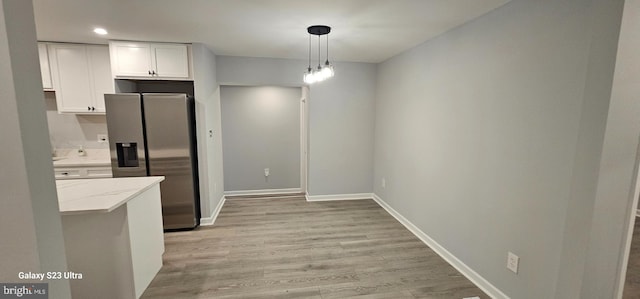 kitchen with white cabinetry, stainless steel fridge, light wood-type flooring, pendant lighting, and light stone counters