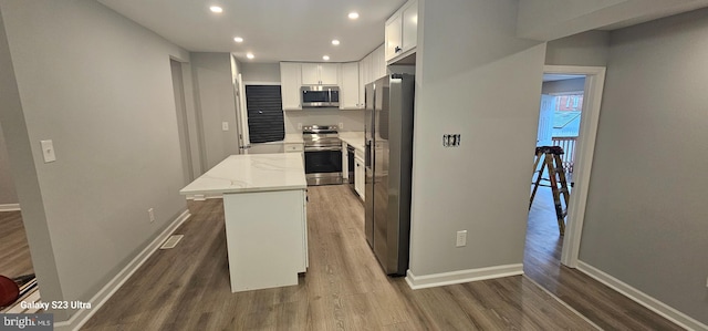 kitchen featuring white cabinetry, stainless steel appliances, dark hardwood / wood-style flooring, light stone countertops, and a kitchen island