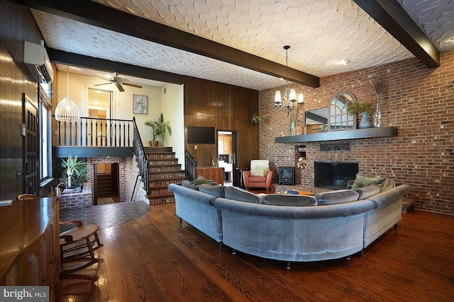 living room featuring a wall unit AC, brick wall, hardwood / wood-style floors, ceiling fan with notable chandelier, and beamed ceiling