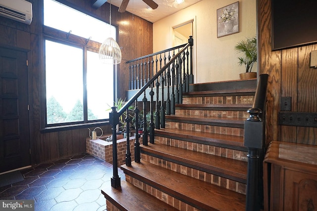 stairway with ceiling fan, a wall mounted air conditioner, and wooden walls