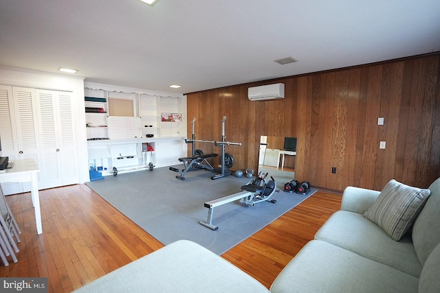 exercise area featuring a wall mounted AC, wooden walls, and hardwood / wood-style flooring