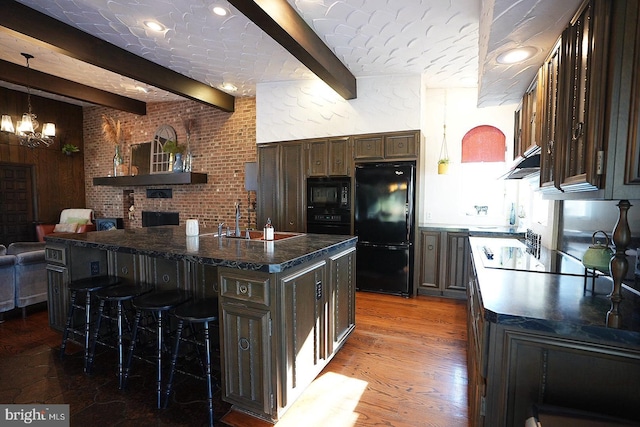 kitchen with sink, a kitchen breakfast bar, an island with sink, black appliances, and beam ceiling