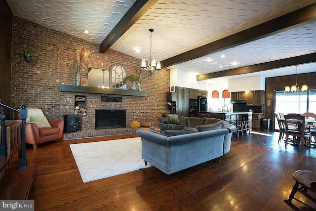 living room featuring brick wall, dark wood-type flooring, an inviting chandelier, and beamed ceiling