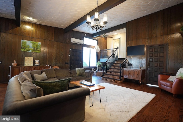 living room featuring an AC wall unit, dark hardwood / wood-style floors, wood walls, beam ceiling, and ceiling fan with notable chandelier