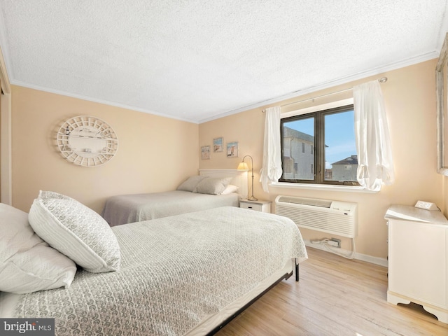 bedroom featuring ornamental molding, a textured ceiling, a wall unit AC, and light hardwood / wood-style floors