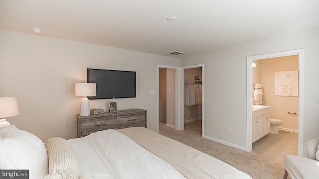 bedroom featuring ensuite bathroom, a spacious closet, a closet, and light colored carpet