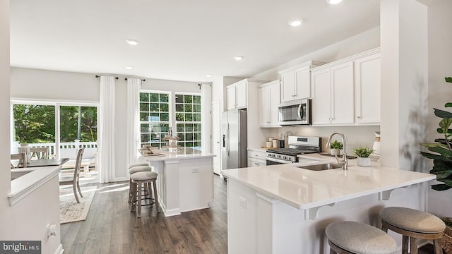 kitchen with a kitchen island with sink, sink, appliances with stainless steel finishes, a kitchen bar, and white cabinetry