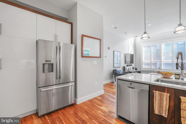 kitchen with sink, decorative light fixtures, appliances with stainless steel finishes, light hardwood / wood-style floors, and white cabinets