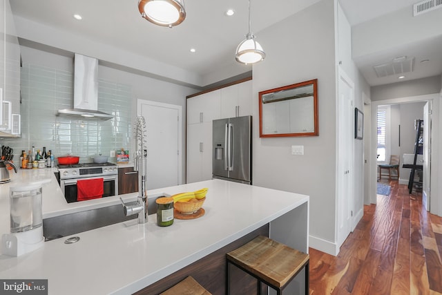 kitchen featuring wall chimney range hood, dark hardwood / wood-style floors, pendant lighting, stainless steel appliances, and white cabinets