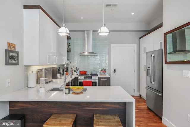 kitchen with wall chimney exhaust hood, kitchen peninsula, pendant lighting, stainless steel appliances, and white cabinets