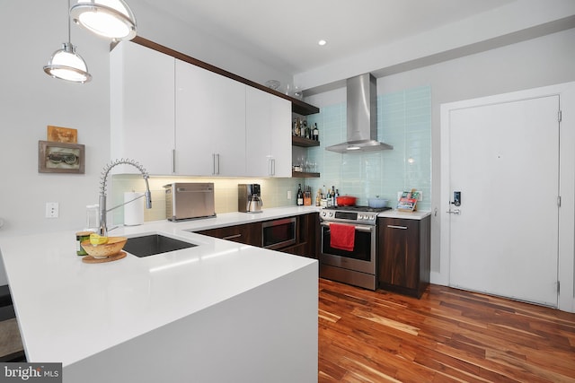 kitchen featuring appliances with stainless steel finishes, decorative light fixtures, white cabinetry, sink, and wall chimney range hood